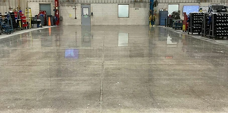Concrete polishing—industrial floor with a smooth, glossy finish reflecting overhead lights in a workshop area.