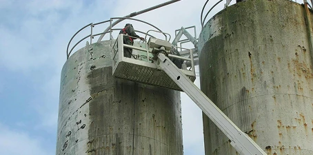 Corrosion control—worker in a lift applying treatment to the surface of large outdoor storage silos.